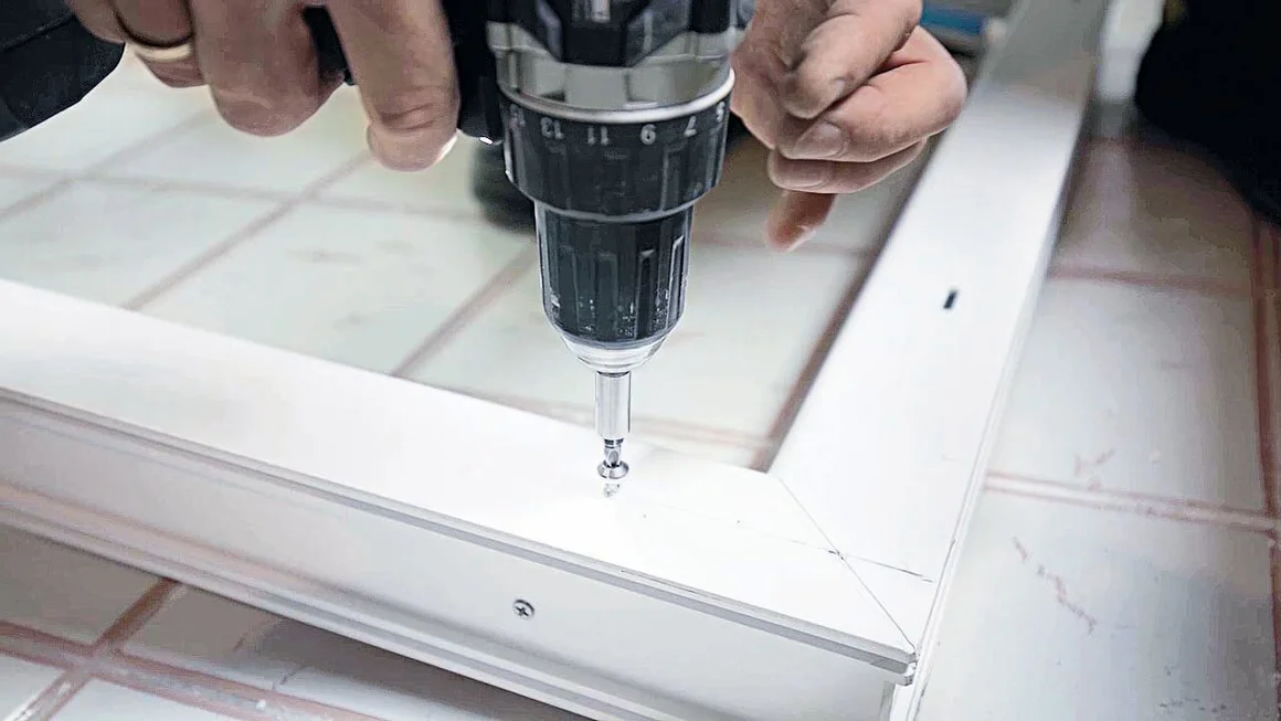 Person verschraubt Fensterrahmen mit Akkuschrauber.